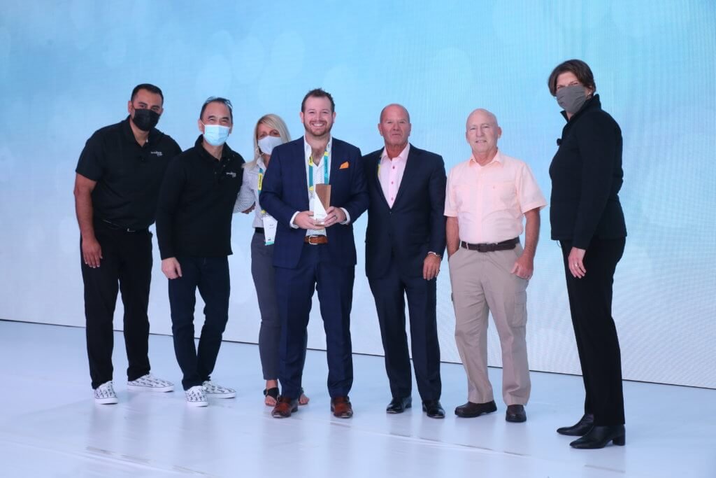 An award winner holding a plaque with corporate presenters