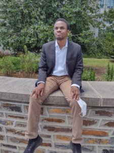 Scholarship recipient Ekene, Okonkwoaguolu sitting on a wall dressed in business attire